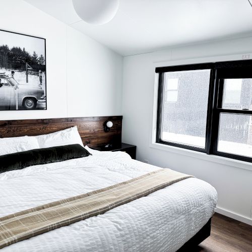 A cozy bedroom with a large bed, white linens, a window, and a black-and-white photo on the wall.