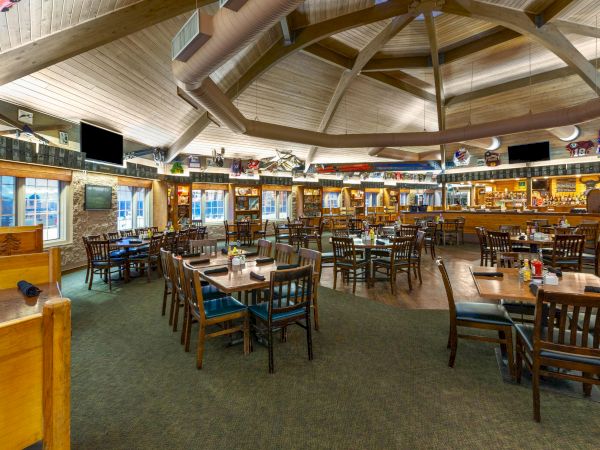 The image shows a spacious, rustic-style restaurant or bar with wooden furniture, tables set, and a visible bar area in the background.