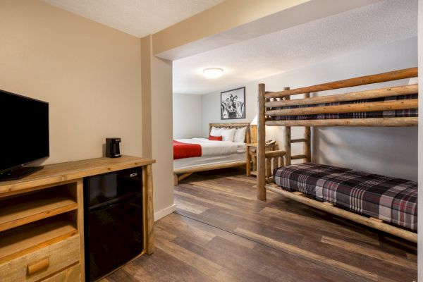 The image shows a cozy bedroom with a bunk bed, a king bed, a TV on a wooden dresser, and a mini-fridge, all set in a neatly organized space.