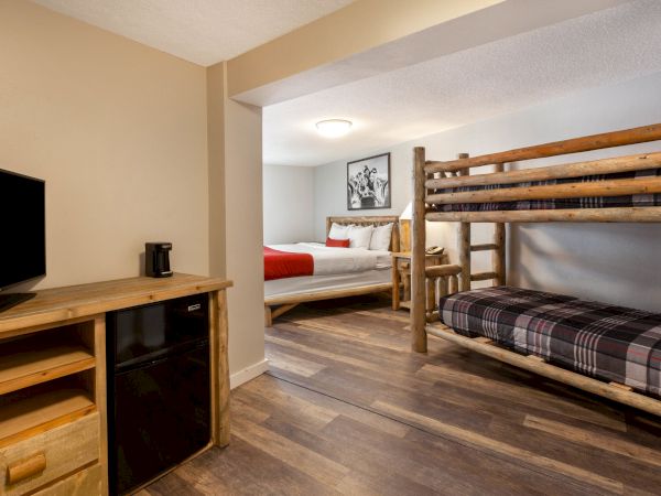 The image shows a cozy bedroom with a bunk bed, a king bed, a TV on a wooden dresser, and a mini-fridge, all set in a neatly organized space.