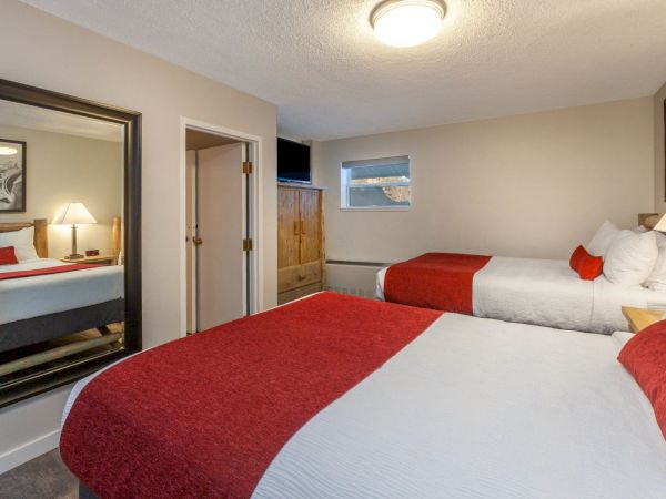 A hotel room with two beds, each covered with white sheets and red blankets, a large mirror, a wardrobe, and two paintings on the walls.