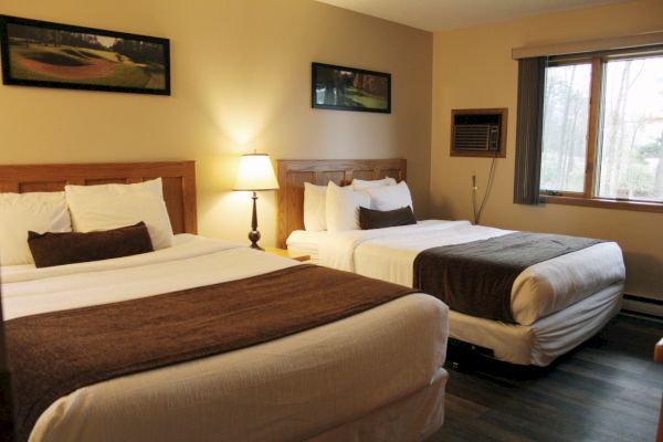 A cozy hotel room with two double beds, stylish wooden headboards, bedside lamp, wall art, and a window bringing in natural light.