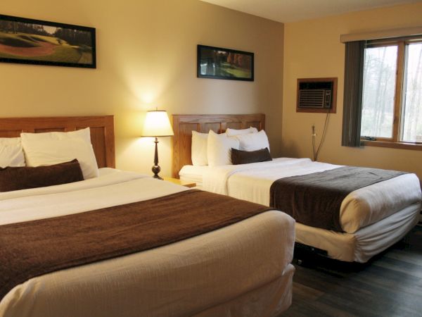 A cozy hotel room with two double beds, stylish wooden headboards, bedside lamp, wall art, and a window bringing in natural light.