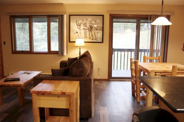 This image shows a cozy living room and dining area with wooden furniture, a couch, a coffee table, and a framed picture on the wall.