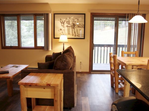 This image shows a cozy living room and dining area with wooden furniture, a couch, a coffee table, and a framed picture on the wall.