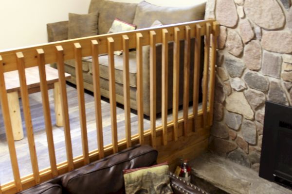 The image shows a split-level living area with a stone fireplace, couches on both levels, wooden railing, and windows allowing natural light.