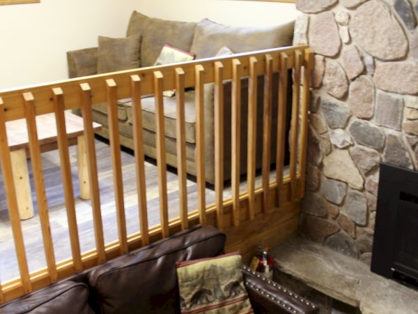 The image shows a split-level living area with a stone fireplace, couches on both levels, wooden railing, and windows allowing natural light.