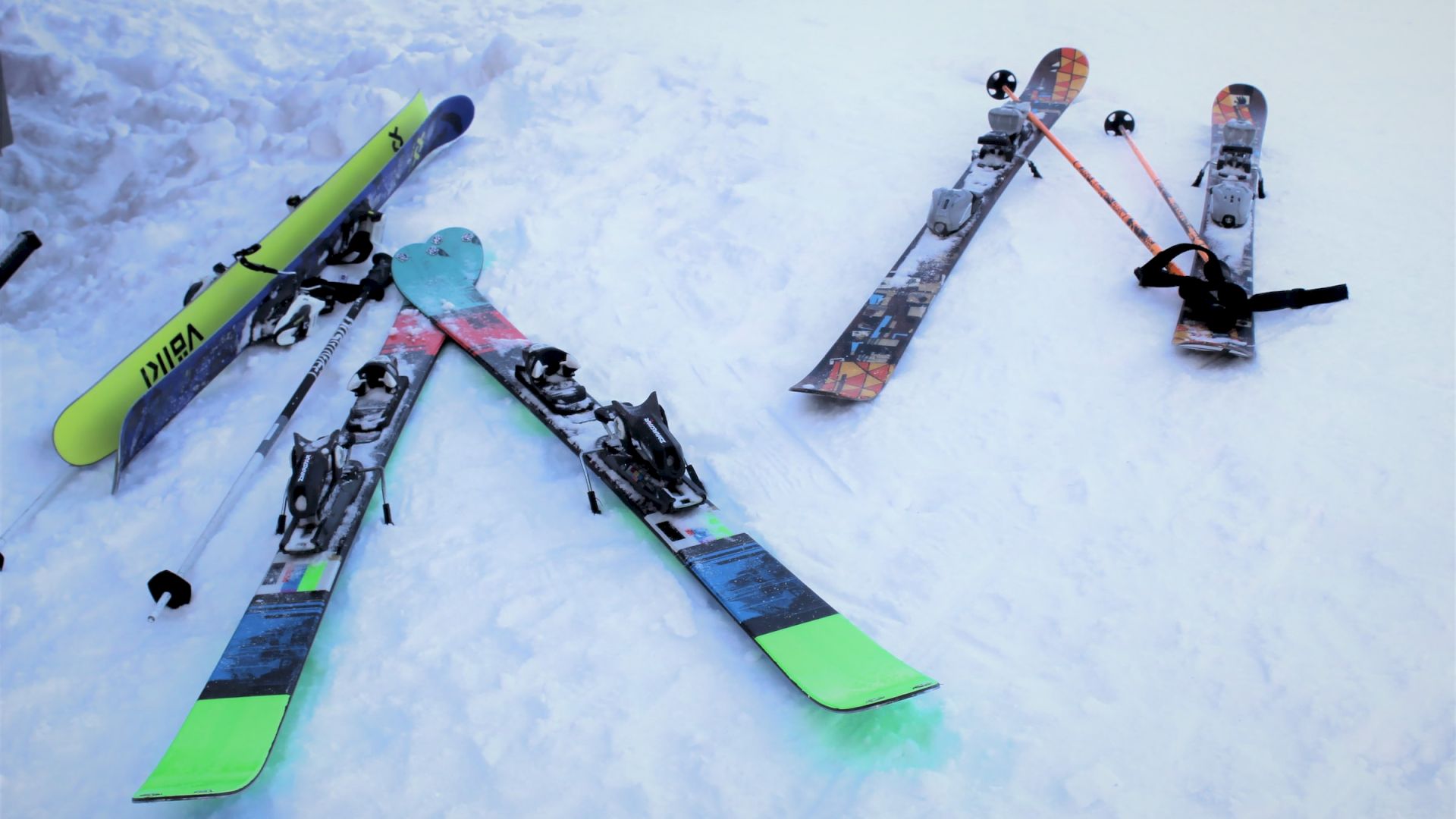 The image shows three sets of skis, with their bindings visible, placed on a snowy surface, set against a snowy backdrop.