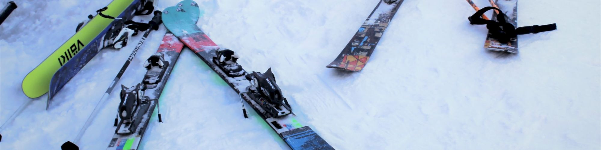 The image shows three sets of skis, with their bindings visible, placed on a snowy surface, set against a snowy backdrop.