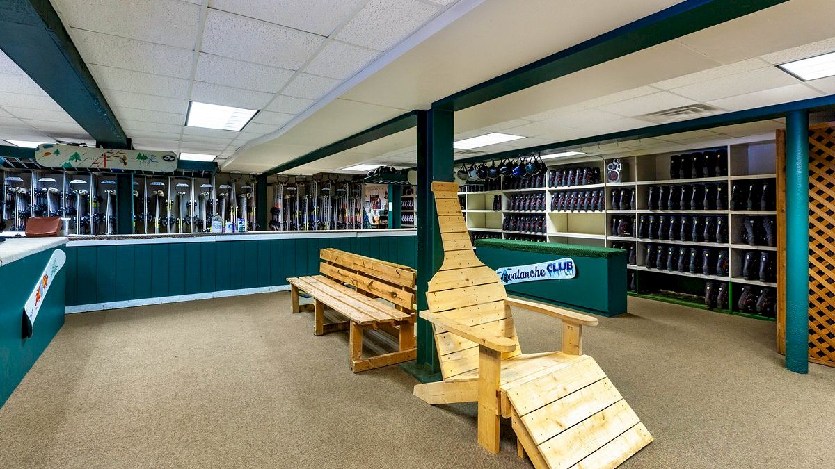 The image shows an indoor area with shelves full of ice skates and colorful benches. A prominent wooden display resembling a ski is in the center.