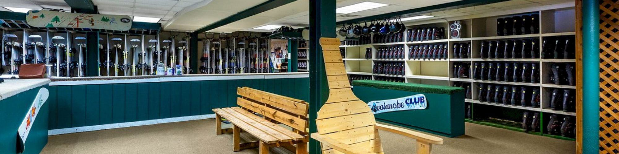 The image shows an indoor area with shelves full of ice skates and colorful benches. A prominent wooden display resembling a ski is in the center.