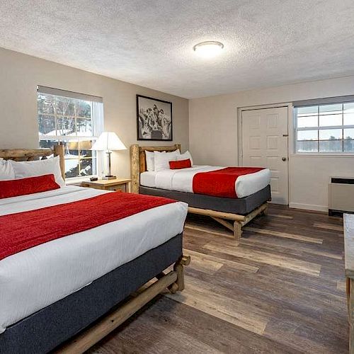 A modern hotel room with two queen-sized beds, red accents, a TV, and a window. A door leads outside and a picture hangs on the wall.