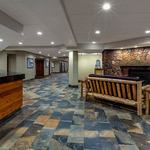 A spacious, well-lit lobby features a reception desk, wooden furniture, a stone fireplace, and tiled flooring in an inviting layout.