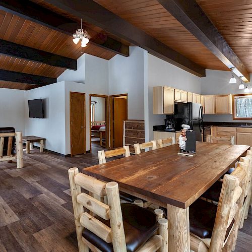 This image features a rustic open-concept kitchen and dining area with wooden furniture, exposed beams, and hardwood floors, creating a cozy cabin vibe.