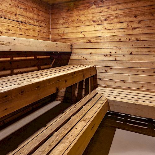 The image shows the interior of a wooden sauna with multiple bench levels, wooden walls, and soft lighting.