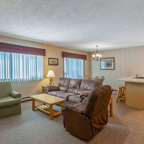 A cozy living room with a sofa, armchairs, coffee table, and a lamp, adjacent to a dining area and a kitchen island with bar stools ending the sentence.