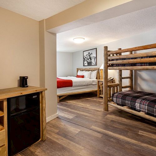 The image shows a cozy bedroom with a bunk bed, a double bed, wooden furniture, a TV, and a mini-fridge, all in a warmly lit space.