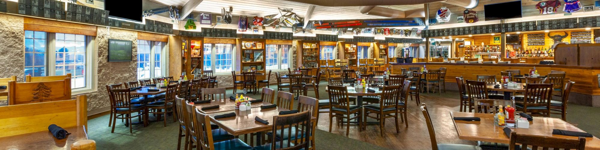 The image shows a spacious, wooden-furnished restaurant with tables, chairs, a bar, ceiling beams, and decorative items.