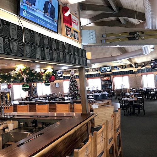 The image shows the interior of a restaurant with a bar area, Christmas decorations, and multiple televisions. Tables and chairs are arranged.