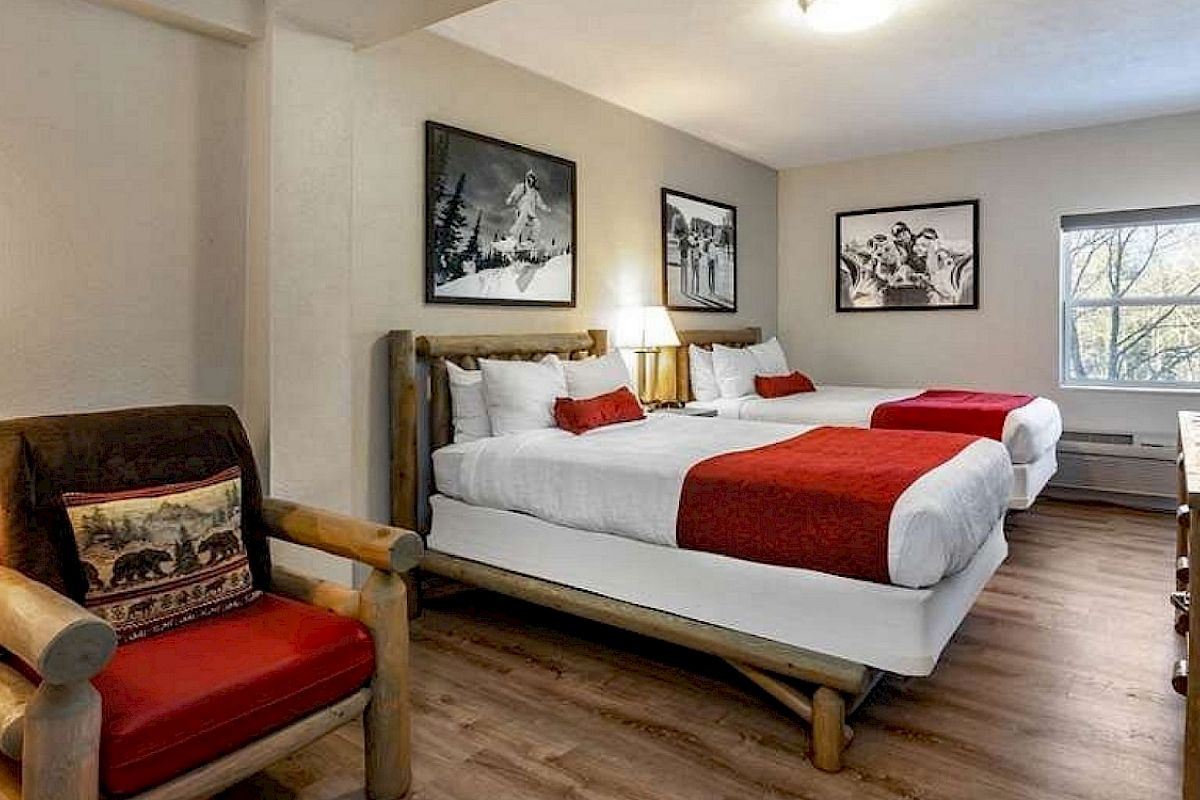 A cozy hotel room with two double beds, red accents, armchair, nature-themed decor, wall art, wooden flooring, and a TV near the window.