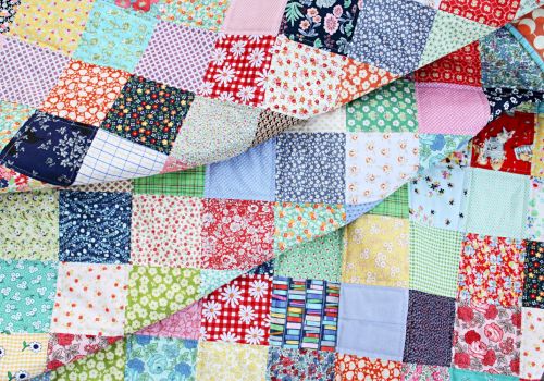 The image shows a colorful patchwork quilt made of many squares with various patterns and colors, including florals, plaids, and solids.