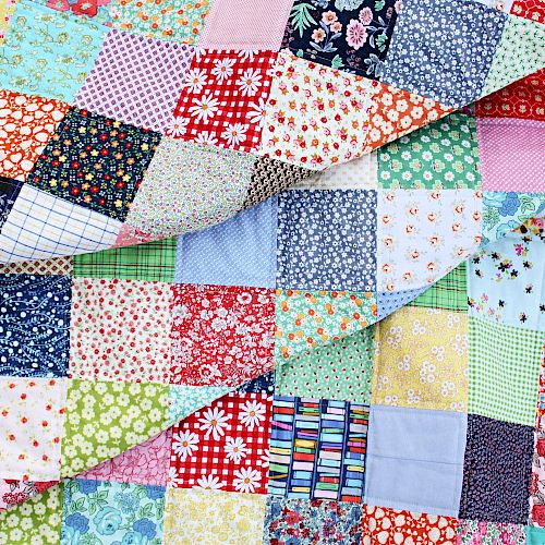 The image shows a colorful patchwork quilt made of many squares with various patterns and colors, including florals, plaids, and solids.