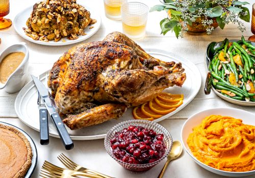 A table set for a festive meal with a roasted turkey, green beans, cranberries, sweet potatoes, stuffing, pie, and gravy.