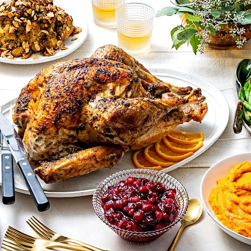 A table set for a festive meal with a roasted turkey, green beans, cranberries, sweet potatoes, stuffing, pie, and gravy.