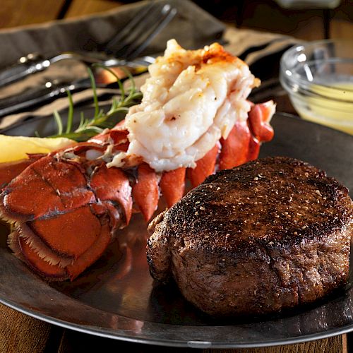 A plate featuring a juicy steak and a buttered lobster tail, garnished with a lemon wedge and rosemary, with a small bowl of melted butter on the side.