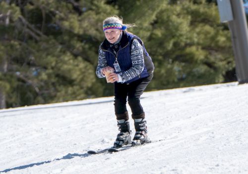 A person skiing downhill on a snowy slope, wearing winter clothing, with trees in the background and a ski pole or sign visible.