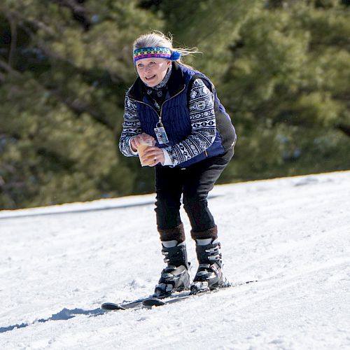 A person skiing downhill on a snowy slope, wearing winter clothing, with trees in the background and a ski pole or sign visible.