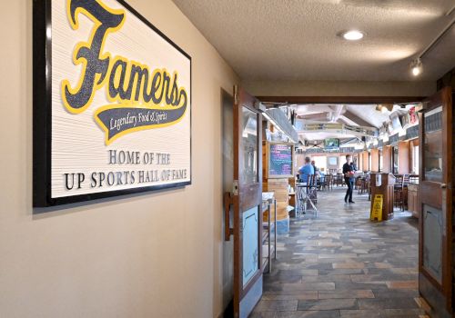 A hallway leads to a restaurant with a sign on the wall reading, "Famers Legendary Food & Spirits, Home of the UP Sports Hall of Fame."