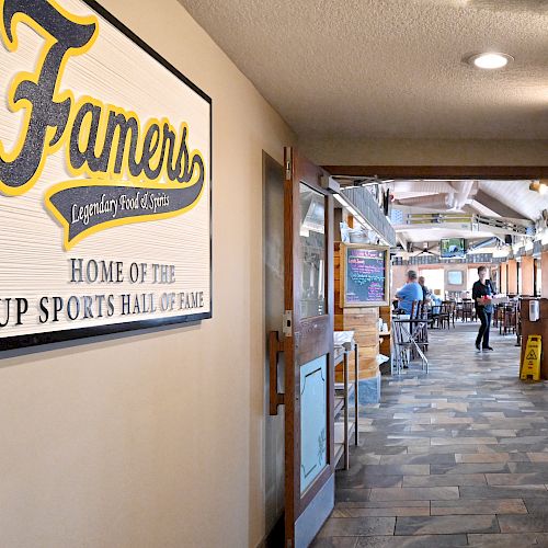 A hallway leads to a restaurant with a sign on the wall reading, "Famers Legendary Food & Spirits, Home of the UP Sports Hall of Fame."