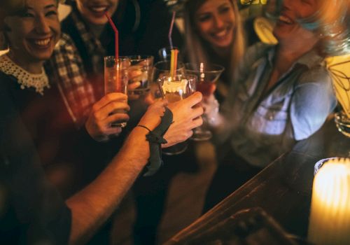 A group of people laughing and toasting drinks at a bar, with a warm atmosphere and a candlelit setting.