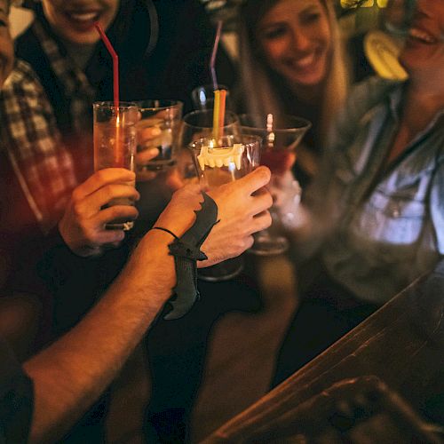 A group of people laughing and toasting drinks at a bar, with a warm atmosphere and a candlelit setting.