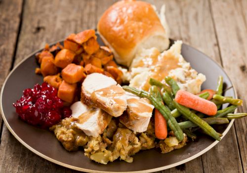 A plate with turkey, stuffing, cranberry sauce, sweet potatoes, green beans with carrots, mashed potatoes, and a dinner roll.