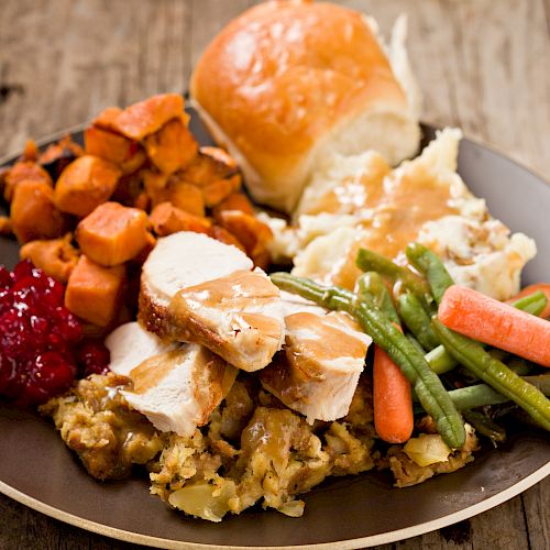 A plate with turkey, stuffing, cranberry sauce, sweet potatoes, green beans with carrots, mashed potatoes, and a dinner roll.