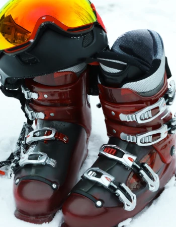 A pair of red ski boots and a ski helmet with goggles rest on snow, ready for winter sports activities.