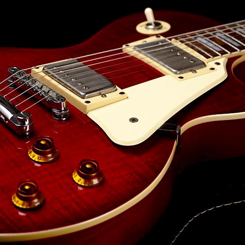 A close-up of a red electric guitar with a white pickguard and four control knobs is shown.