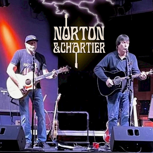 Two musicians are performing on stage with guitars. The backdrop displays "Norton & Chartier" with a lightning design above.
