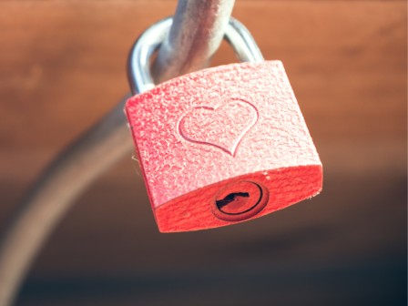 The image shows a red padlock with a heart design, fastened onto a cable or railing, symbolizing love or commitment.