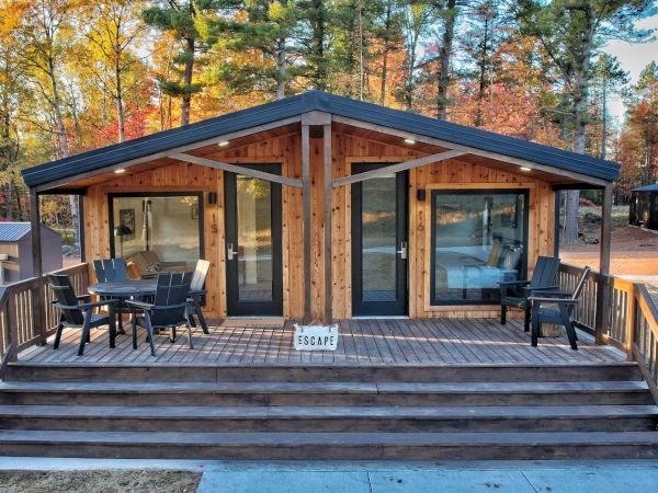 A wooden cabin with a porch, surrounded by trees, and outdoor furniture.