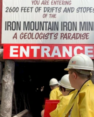 People in yellow jackets and helmets entering the Iron Mountain Iron Mine, a geological site with 2600 feet of drifts and stopes.