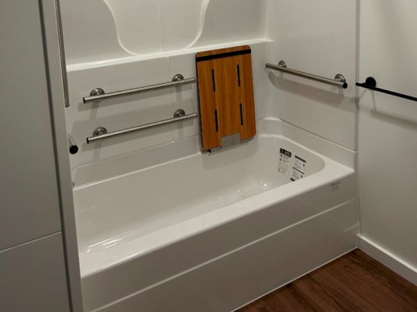 This image shows a white bathtub with stainless steel grab bars and a foldable wooden seat inside.