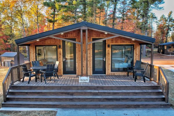 A cozy cabin with a wooden porch surrounded by trees. There's outdoor seating and a small sign that says "ESCAPE" on the steps.