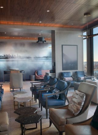A modern lounge with leather seats, a wall mural of a city skyline, and large windows offering a view of a body of water and a Ferris wheel.