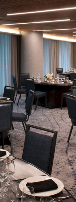 The image shows an elegantly set banquet hall with multiple round tables, black chairs, and dim lighting, ready for an event or dinner.