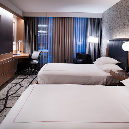 A modern hotel room with two neatly made beds, a flat-screen TV, a desk with a chair, and contemporary decor.