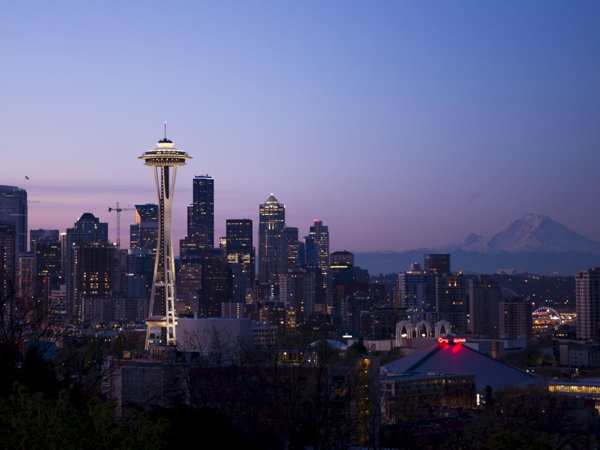 A twilight view of the Seattle skyline with the Space Needle prominently featured and Mount Rainier visible in the background.
